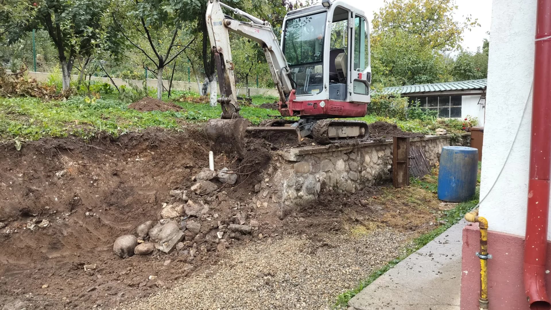 Excavator îndepărtează pământul de lângă un zid de sprijin