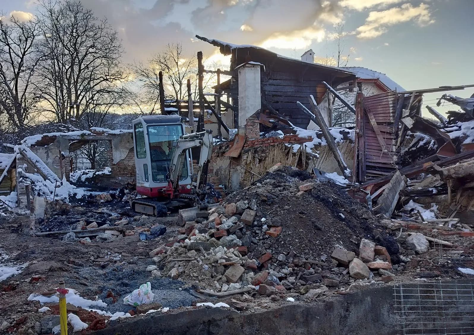 Mini excavator printre resturi arse și moloz după incendiu