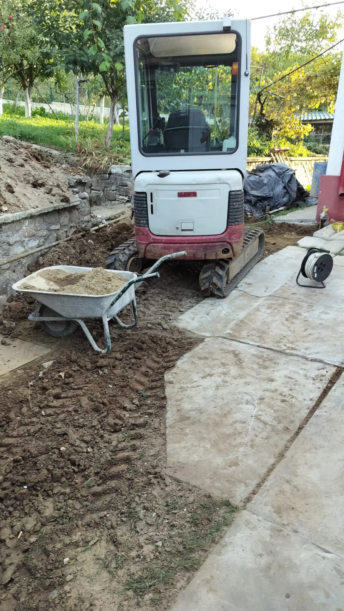 Mini excavator și roabă pe șantier, lângă o săpătură în curte