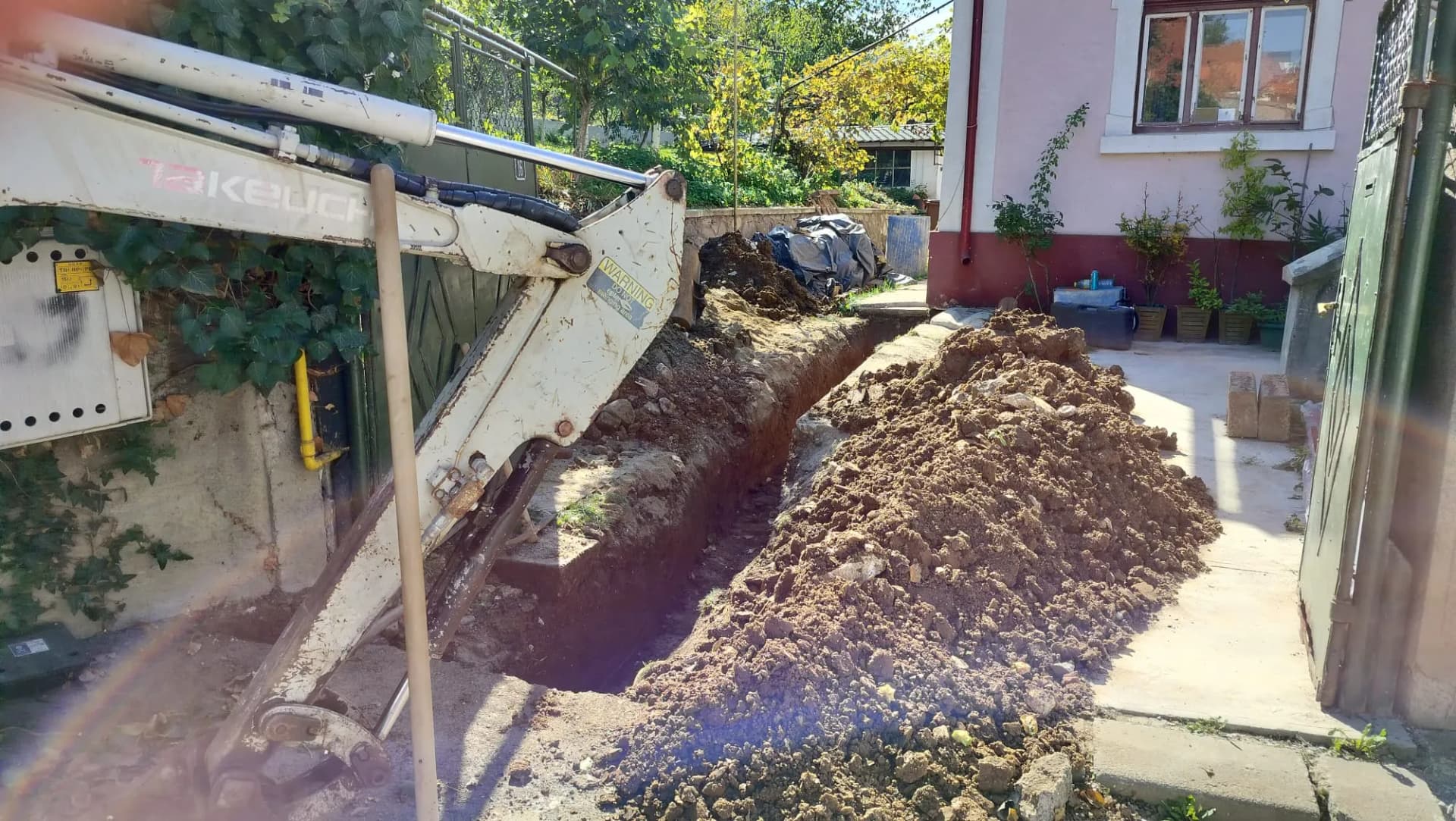 Mini excavator sapă un șanț îngust lângă aleea casei