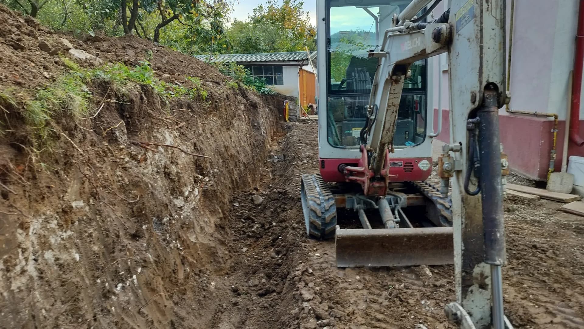 Mini excavator lucrează într-un șanț îngust de-a lungul proprietății