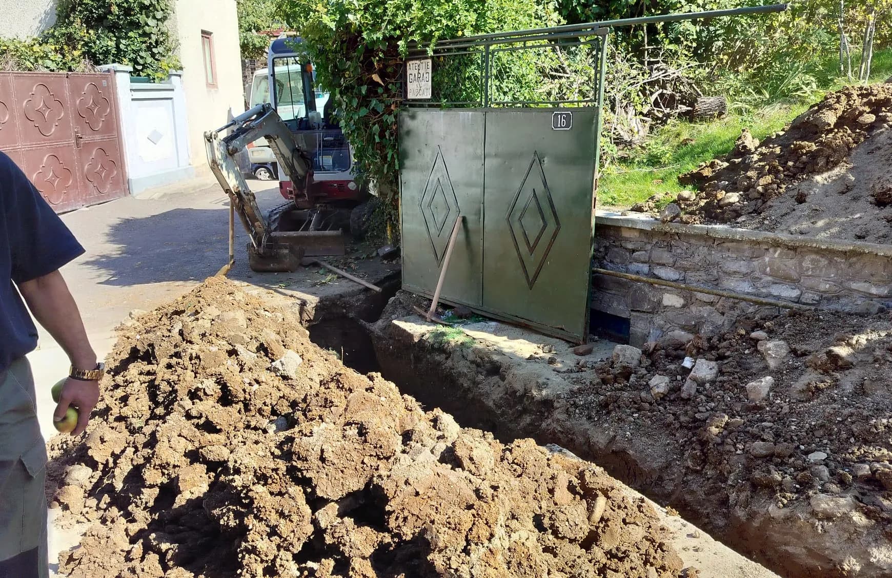 Mini excavator și șanț lung săpat de-a lungul aleii din curte