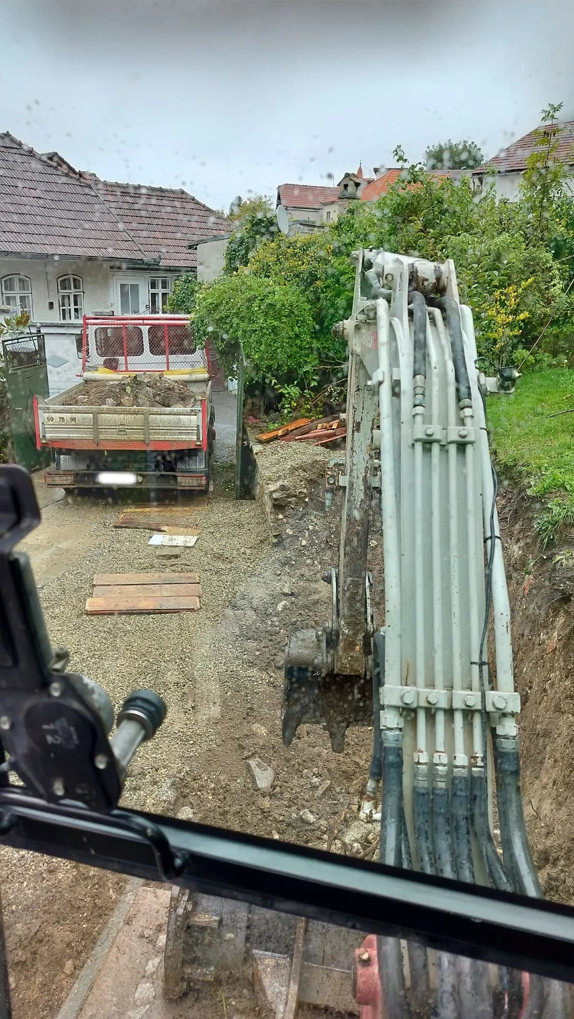 Mini excavator văzut din spate pe șantier, lângă o roabă cu nisip