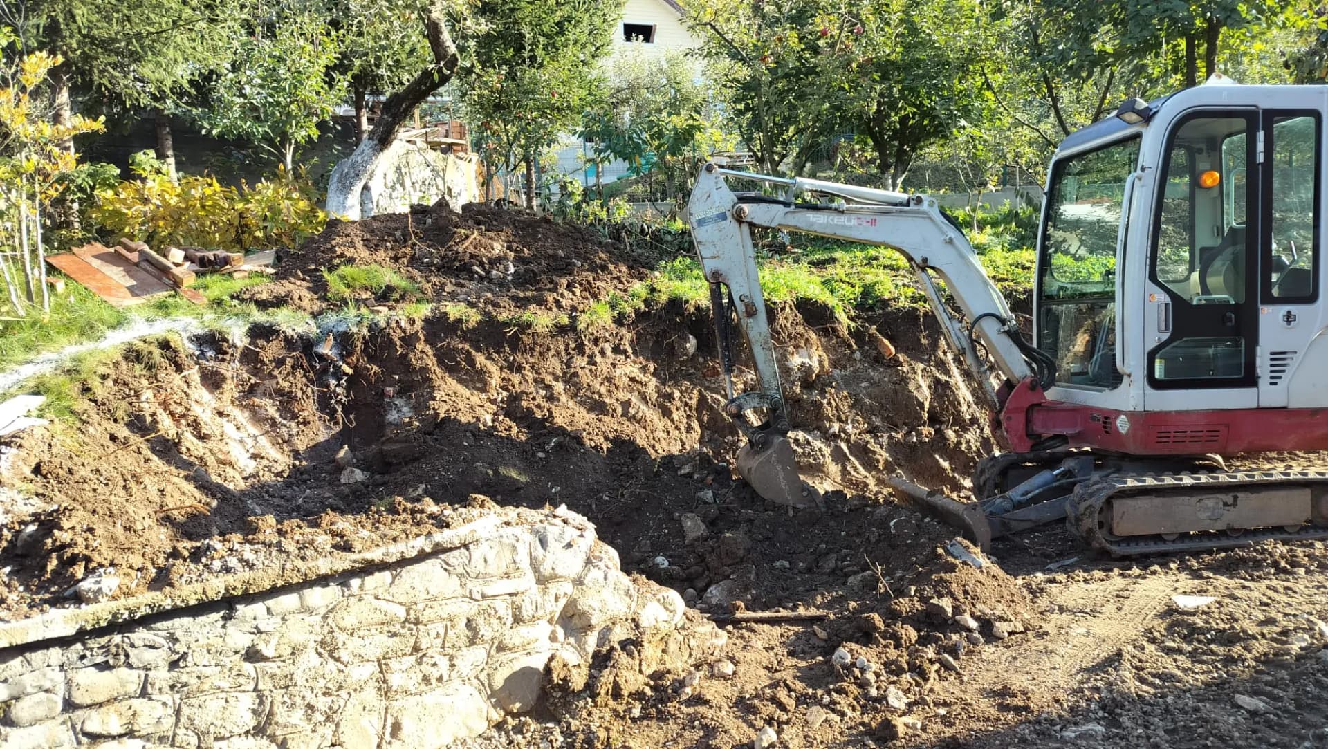 Mini excavator sapă lângă un zid de sprijin din piatră